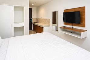 A modern bedroom with a bed, a TV mounted on a wooden panel, and a bathroom with a sink and mirror. - Starla Room Enviro Cikarang by BukaKamar (Cikarang/Bekasi)