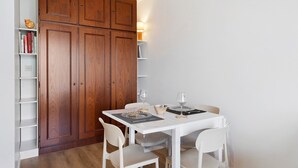 Un comedor con una mesa blanca, cuatro sillas, una copa de vino, un bol y un aparador de madera con libros.