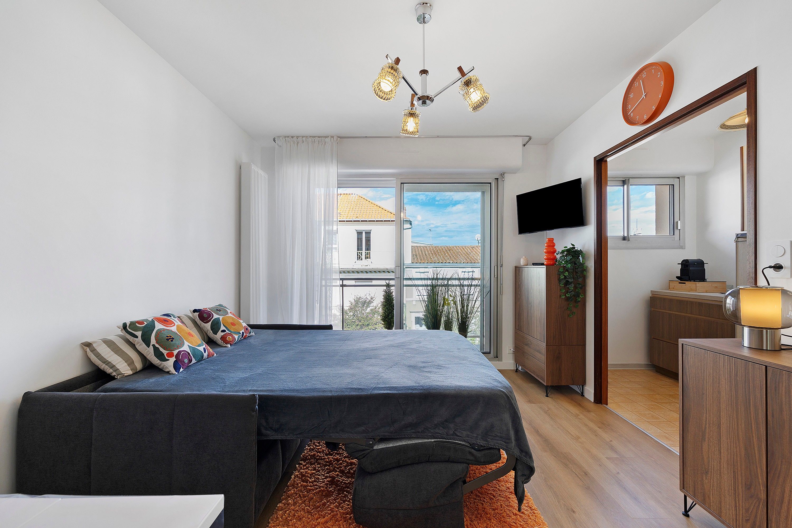 Une chambre avec un lit, une télévision, un miroir et un balcon donnant sur des immeubles.