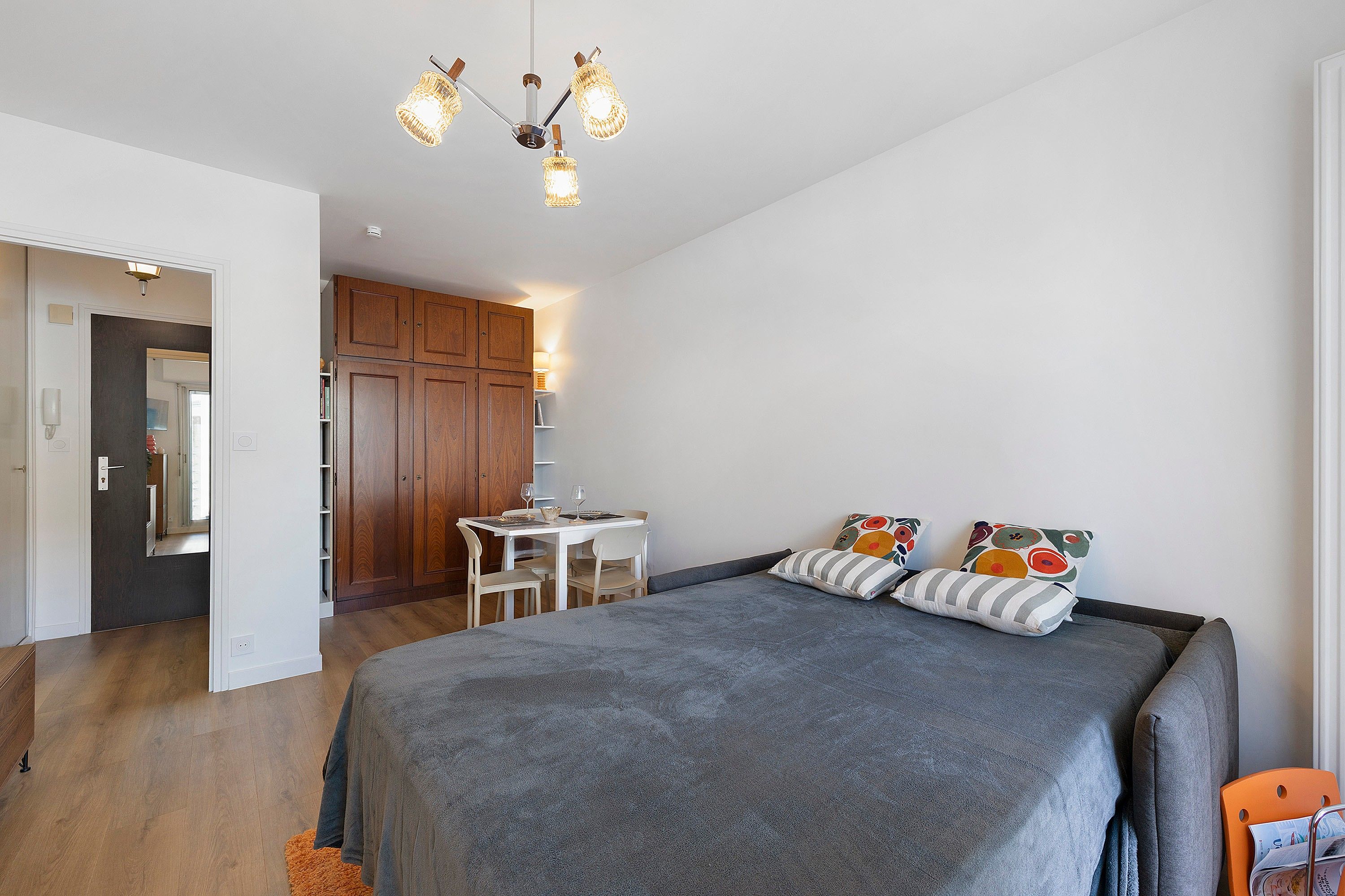A bedroom with a bed, a desk, and a chair. There is a wardrobe and a door leading to another room.