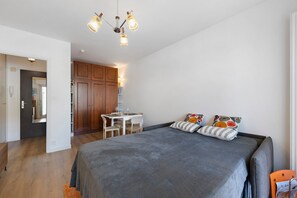 Un dormitorio con cama, escritorio y silla. Hay un armario y una puerta que da a otra habitación.