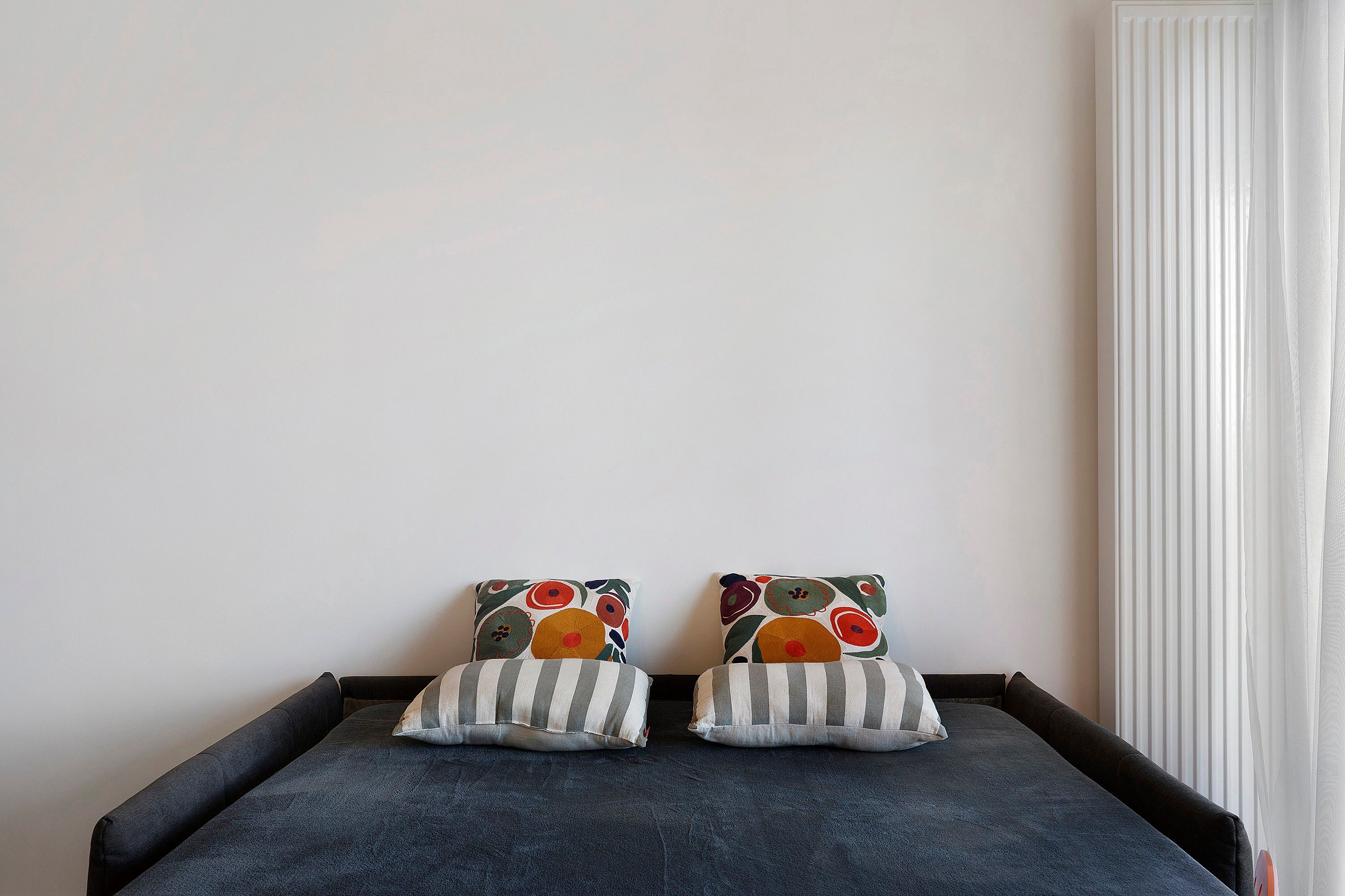A bed with two pillows, one with a floral pattern and the other with stripes, against a plain wall.