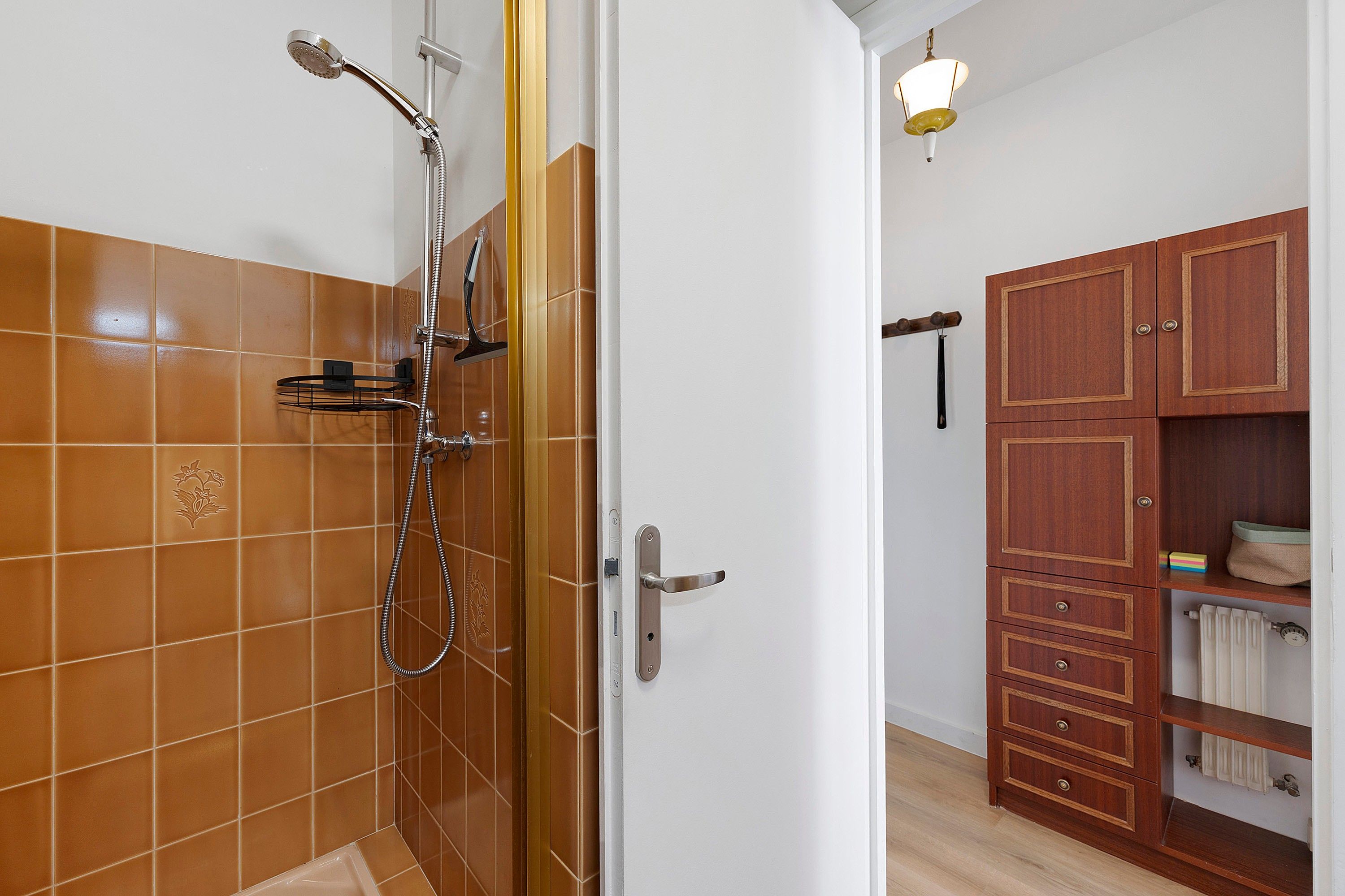 Un bagno con doccia, pareti piastrellate, un armadietto in legno e un corpo illuminante.