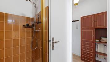Un bagno con doccia, pareti piastrellate, un armadietto in legno e un corpo illuminante.