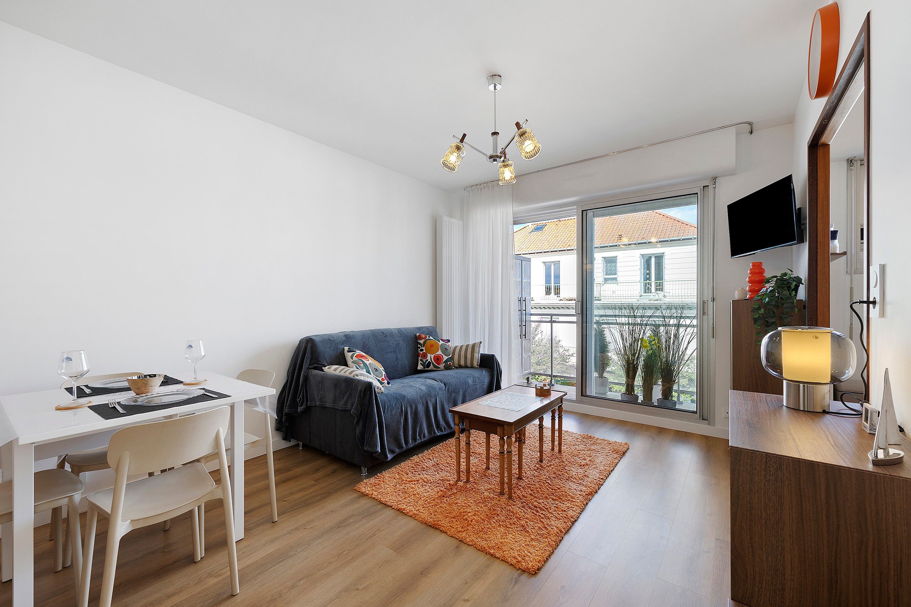 A modern living room with a dining area, a sofa, a coffee table, and a TV mounted on the wall.