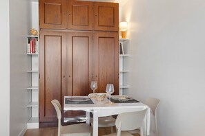 Uma sala de jantar com uma mesa branca, duas cadeiras, um armário de madeira e uma estante de livros.