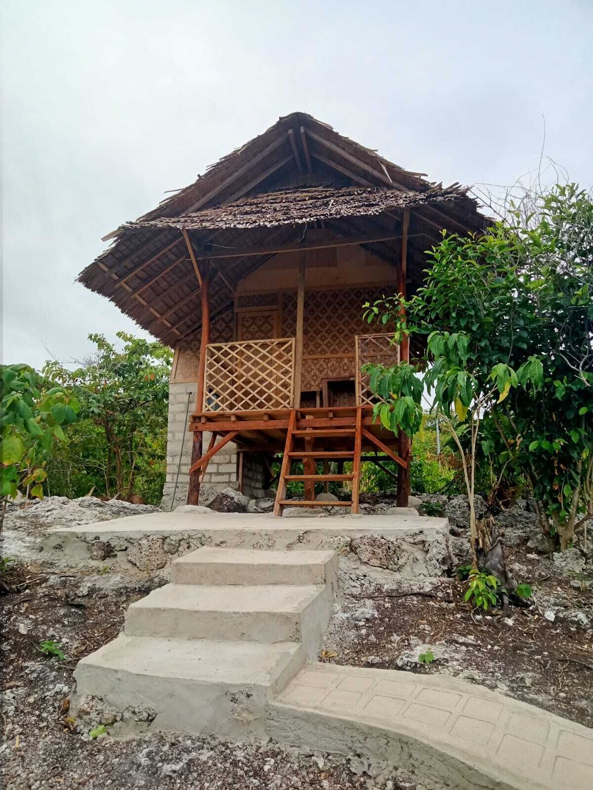 A traditional wooden house with a thatched roof, a wooden balcony, and a stone staircase leading to the entrance.