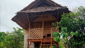Ein traditionelles Holzhaus mit einem Reetdach, einem hölzernen Balkon und einer Steintreppe, die zum Eingang führt.