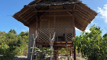 A traditional wooden structure with a thatched roof, surrounded by vegetation and gravel.