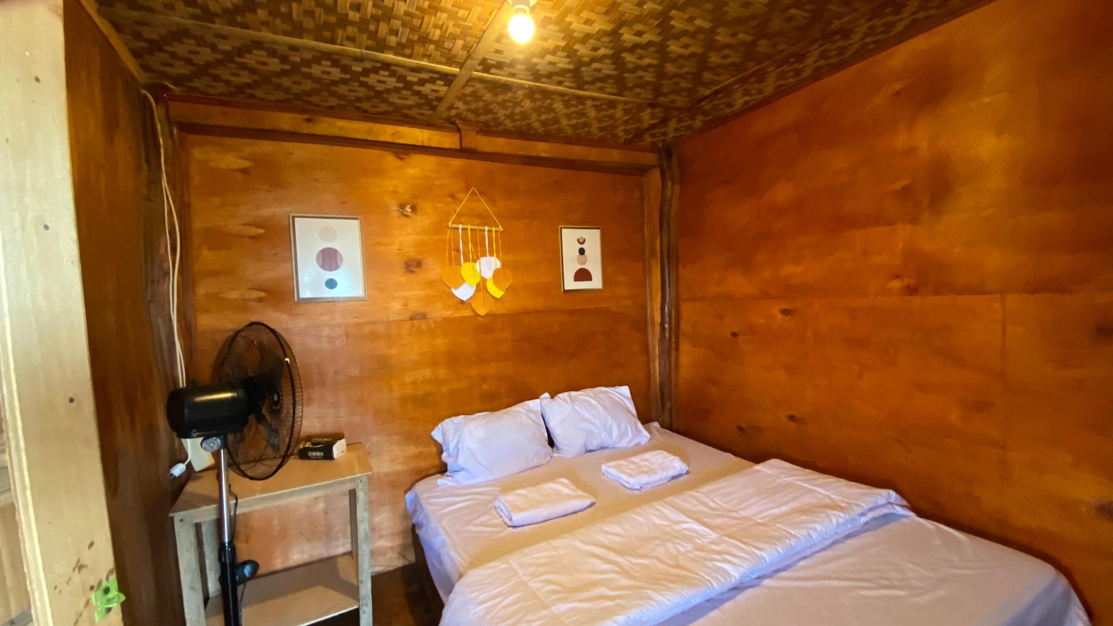 A wooden room with a bed, a bedside table, a fan, and wall decorations.