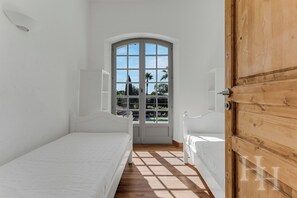 A room with two beds, a wooden door, and a window with a view of palm trees and a swimming pool. - Provençal 4-bedroom house with pool and close to the sea in La Croix-Valmer (La Croix-Valmer)