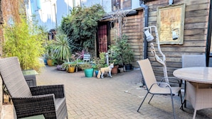 Eine Terrasse im Freien mit Korbmöbeln, Blumentöpfen und einem Hund.