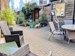 Een terras buiten met rieten meubels, potplanten en een hond.