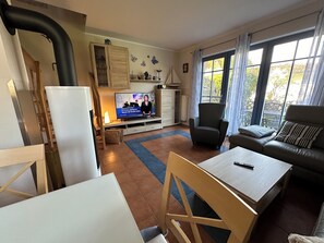 Uma sala de estar com televisão, sofá, mesa e uma cadeira.