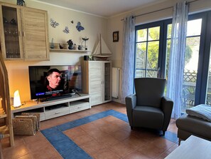 A living room with a television, a sofa, a chair, a cabinet, and a window with curtains. - "Sommerwind" townhouse with 95 square meters of living space and a large, quiet lot (fenced), close to downtown (Zingst)