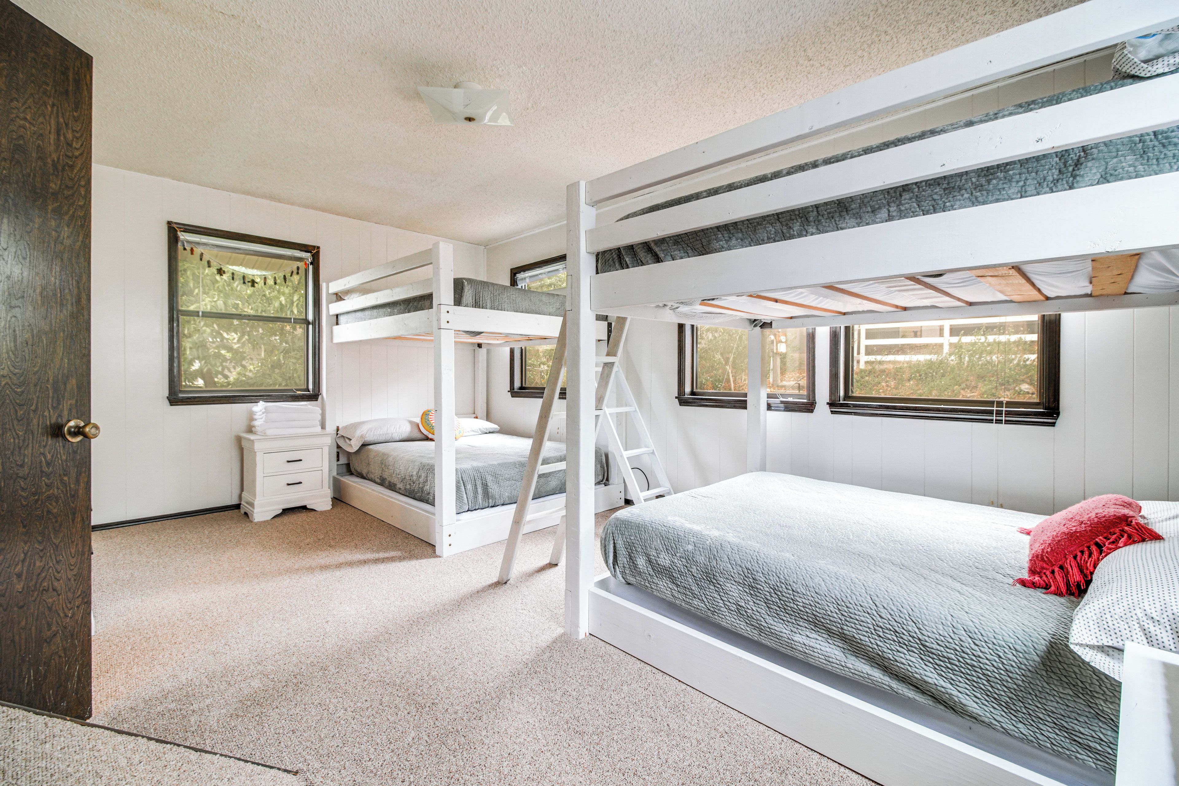 A bunk bed room with a ladder, a small bedside table, and a window.