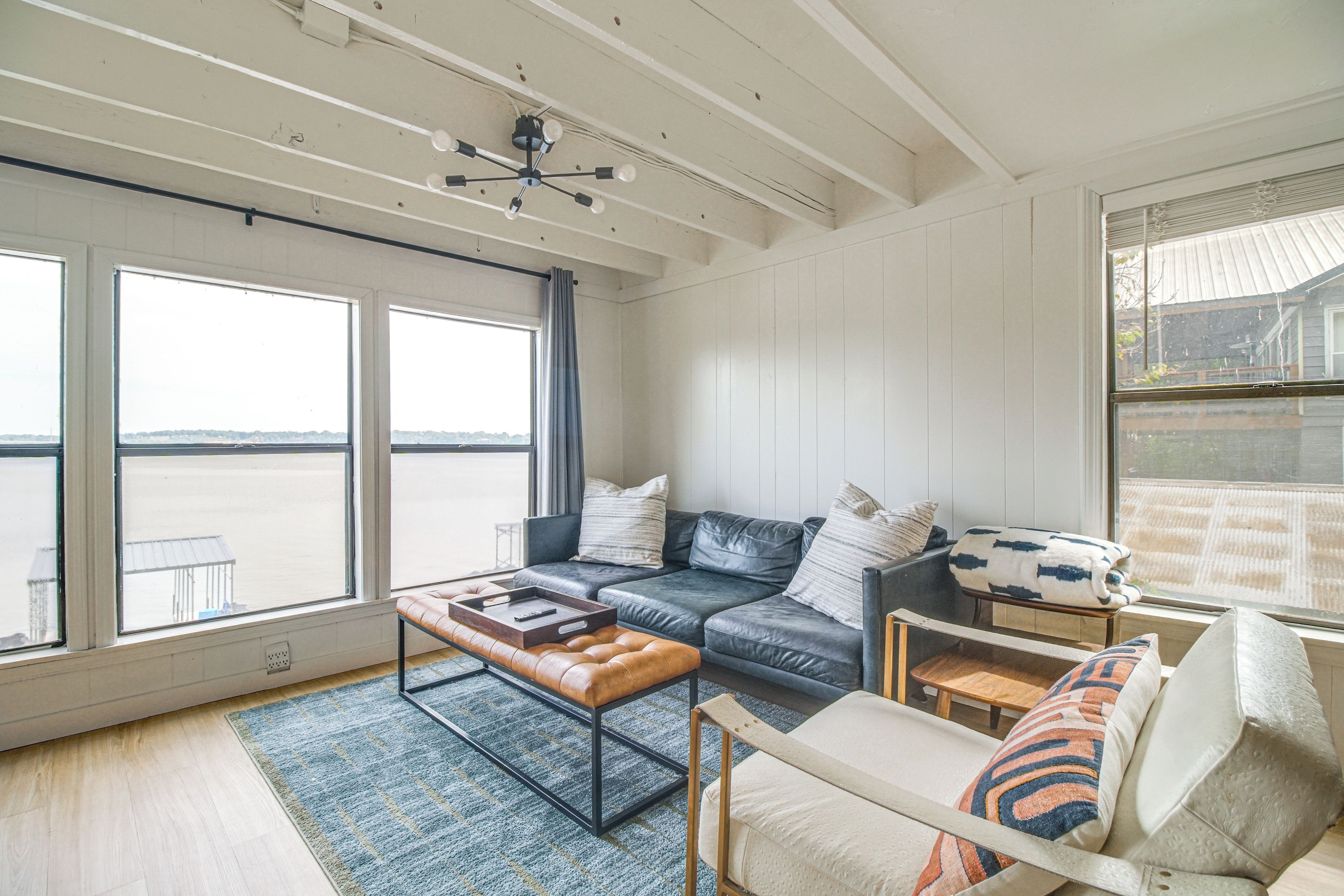 Ein geräumiges Wohnzimmer mit großem Fenster, einem Ledersofa, einem Holztisch und Blick auf das Wasser.