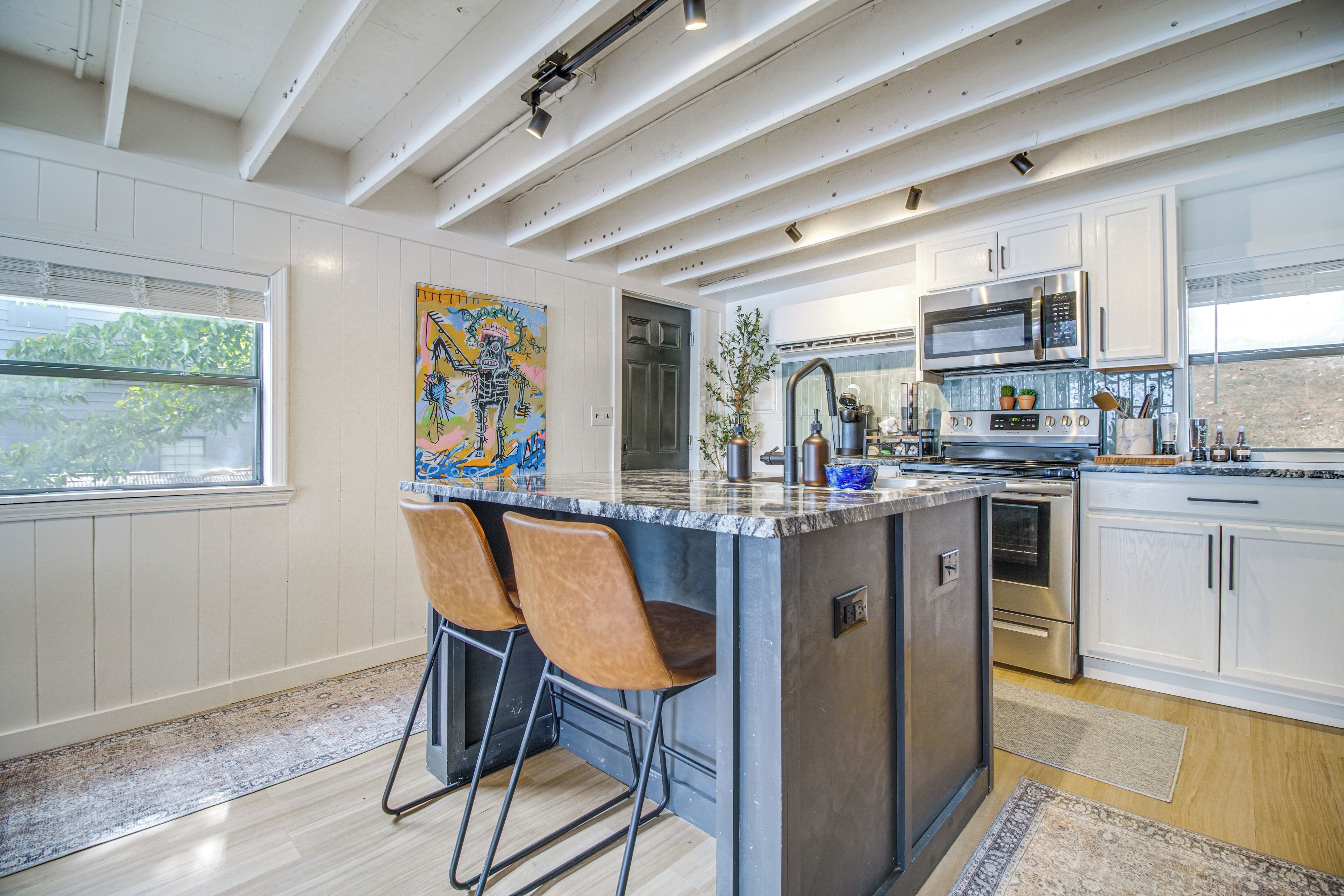 A modern kitchen with a central island, stainless steel appliances, and a large window.