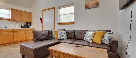 Un espacio de estar moderno con un sofá modular, una mesa de centro de madera y una cocina con armarios de madera y un ventanal.