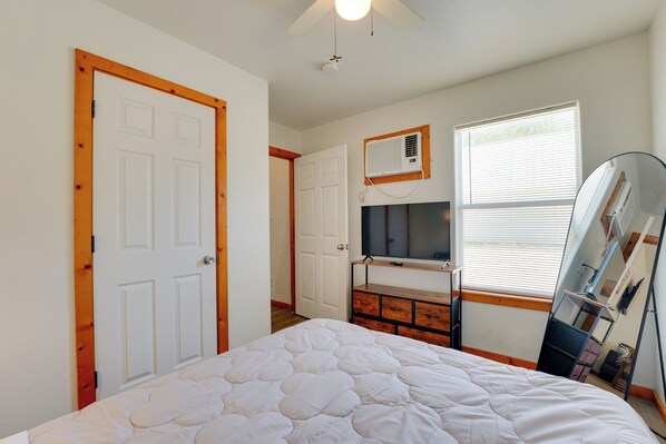 A bedroom with a bed, a TV, a window, and a ceiling fan.