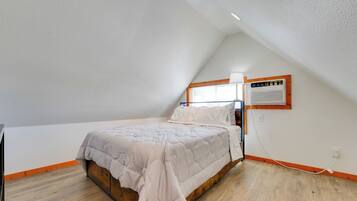 A bedroom with a sloped ceiling, a bed with a wooden frame, a window with blinds, and a wall-mounted air conditioning unit.