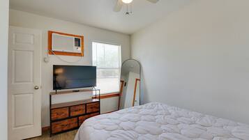 Un dormitorio con una cama, un televisor sobre un mueble de madera, un ventilador de techo y una ventana con persianas.
