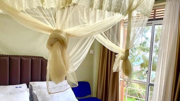Ein Hotelzimmer mit einem großen Bett, einem Baldachin, einem blauen Sessel und Blick auf Grünfläche.