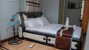 Ein Bett mit einem verzierten Kopfteil, ein Standventilator und eine Fernbedienung auf dem Boden.
