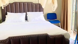 Ein Bett mit Kopfteil, ein blauer Sessel und ein Fenster mit Vorhängen.