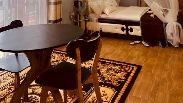 A room with a bed, a table, chairs, a fan, and a window with curtains.