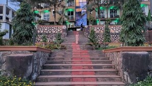 A staircase leading to a building with multiple floors, surrounded by greenery and trees.