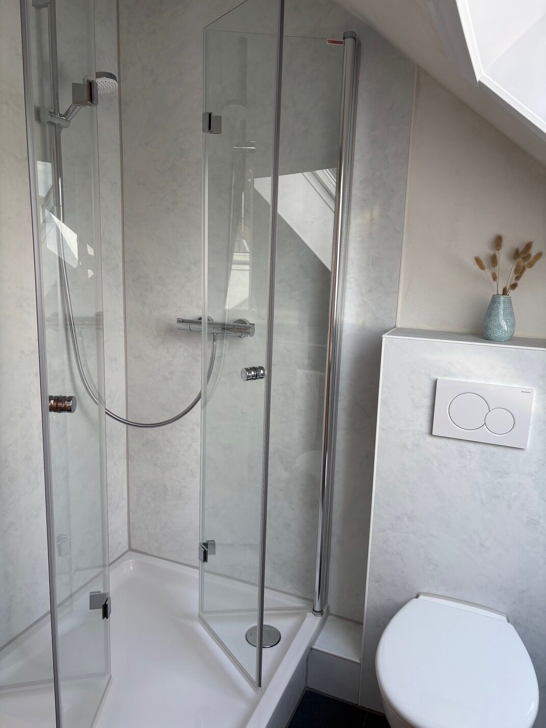 Ein modernes Badezimmer mit einer gläsernen Duschkabine, einer Toilette und einer an der Wand befestigten Bedienkonsole.