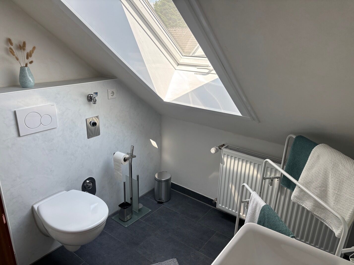 Ein modernes Badezimmer mit Oberlicht, Toilette, Bidet, Heizkörper und Handtuchhalter.