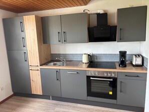 A modern kitchen with grey cabinets, a wooden countertop, a sink, a kettle, a coffee maker, and an oven.