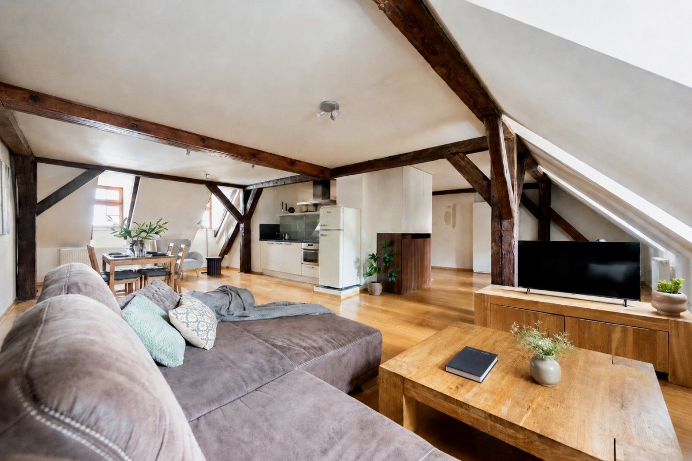 Un espace de vie de style loft avec des poutres en bois apparentes, un canapé, une table basse, un téléviseur et un coin cuisine.