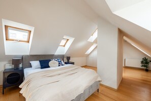 Ein Schlafzimmer mit schrägen Wänden, Oberlichtern, einem Bett mit grauem Kopfteil, Nachttischen und einem Heizkörper.
