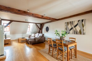 Amplia habitación tipo loft con vigas de madera a la vista, un comedor con mesa y sillas de madera, un sofá y un cuadro abstracto grande en la pared.