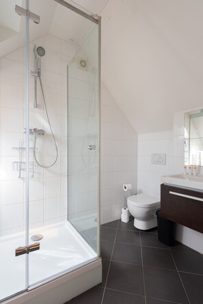 Un baño moderno con ducha envuelta en vidrio, inodoro blanco y tocador de tonos oscuros.