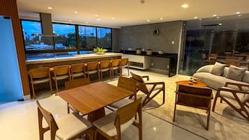 Cozinha moderna com área de refeições, sofás e vista para a paisagem urbana.