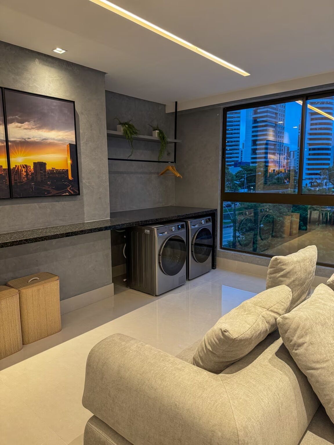 Ein modernes Wohnzimmer mit großem Fenster, einer Couch, einer Waschmaschine und Blick auf die Stadt.