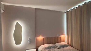 Ett sovrum med en säng, sängbord, en väggmonterad lampa och en gardin.