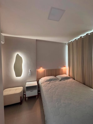 Quarto com cama, mesas de cabeceira, luminária na parede e cortina.