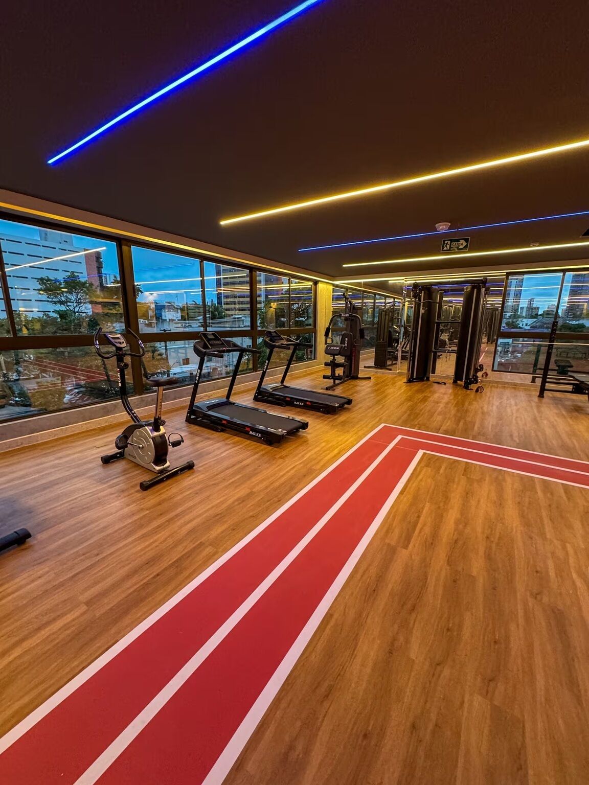 Een fitnessruimte met loopbanden, trainingsapparatuur en grote ramen met uitzicht op de stad.