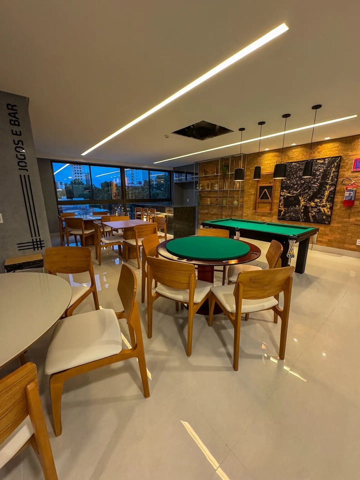Espaço moderno em ambientes internos com mesa de bilhar, vários espaços de estar e vista para a cidade através de grandes janelas.