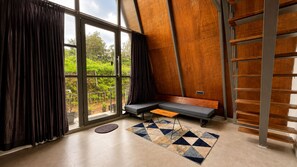A room with a large window, a wooden sloped ceiling, a bench, and a ladder. - Aara Villa (Mahabaleshwar)