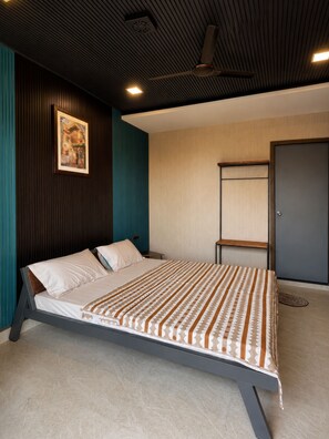 A modern bedroom with a bed, a painting on the wall, and a door. - Aara Villa (Mahabaleshwar)