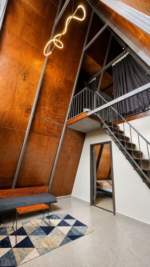 Un interior moderno con techo inclinado de madera, una escalera y un tapete estampado.