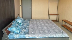 Quarto com cama, porta, um banco e um ventilador de teto.