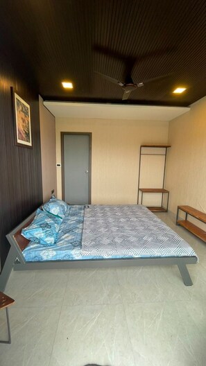 A room with a bed, a door, a bench, and a ceiling fan. - Aara Villa (Satara)