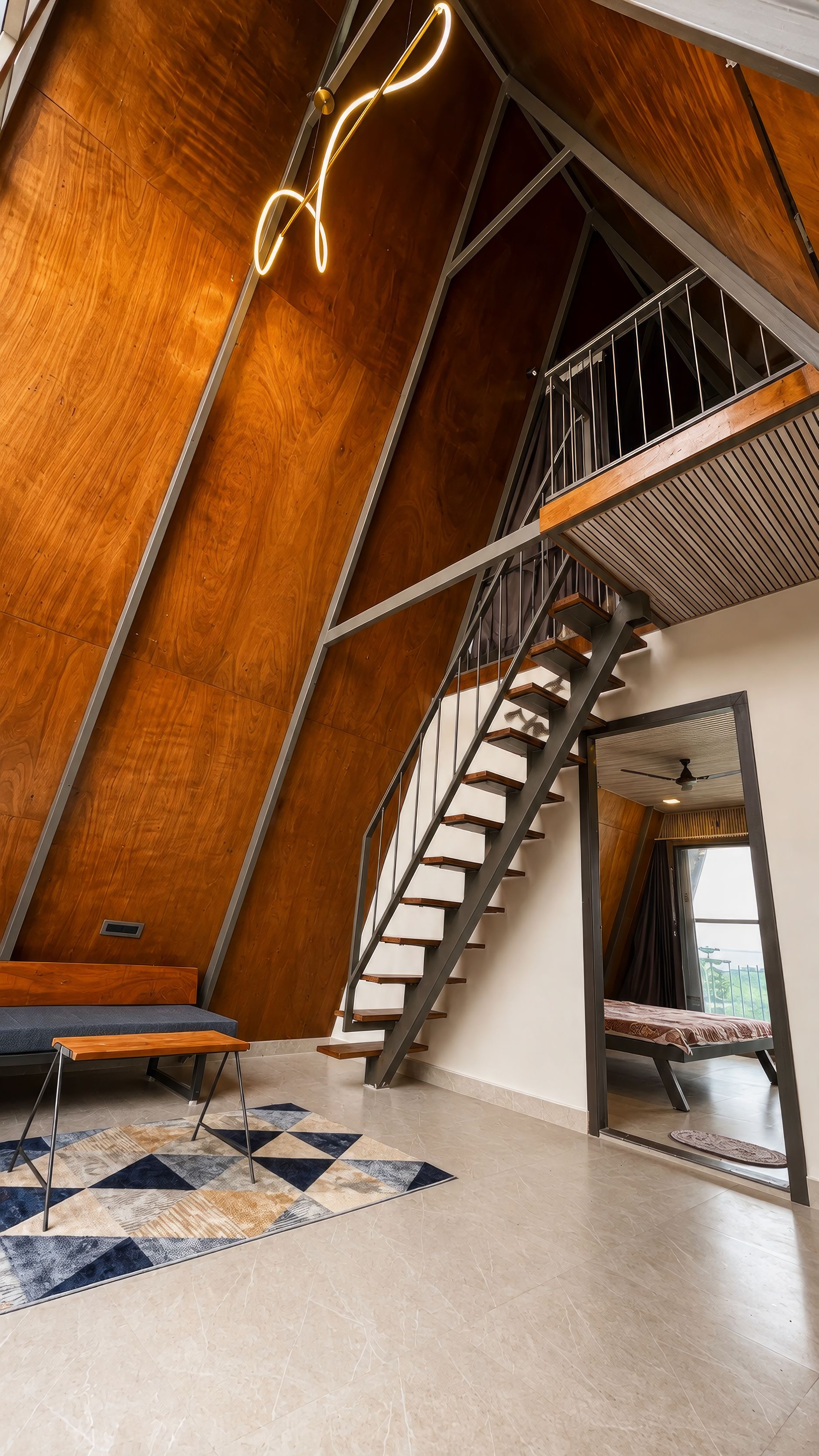 Un interior moderno con techo inclinado de madera, una escalera, una cama y una alfombra con estampado geométrico.